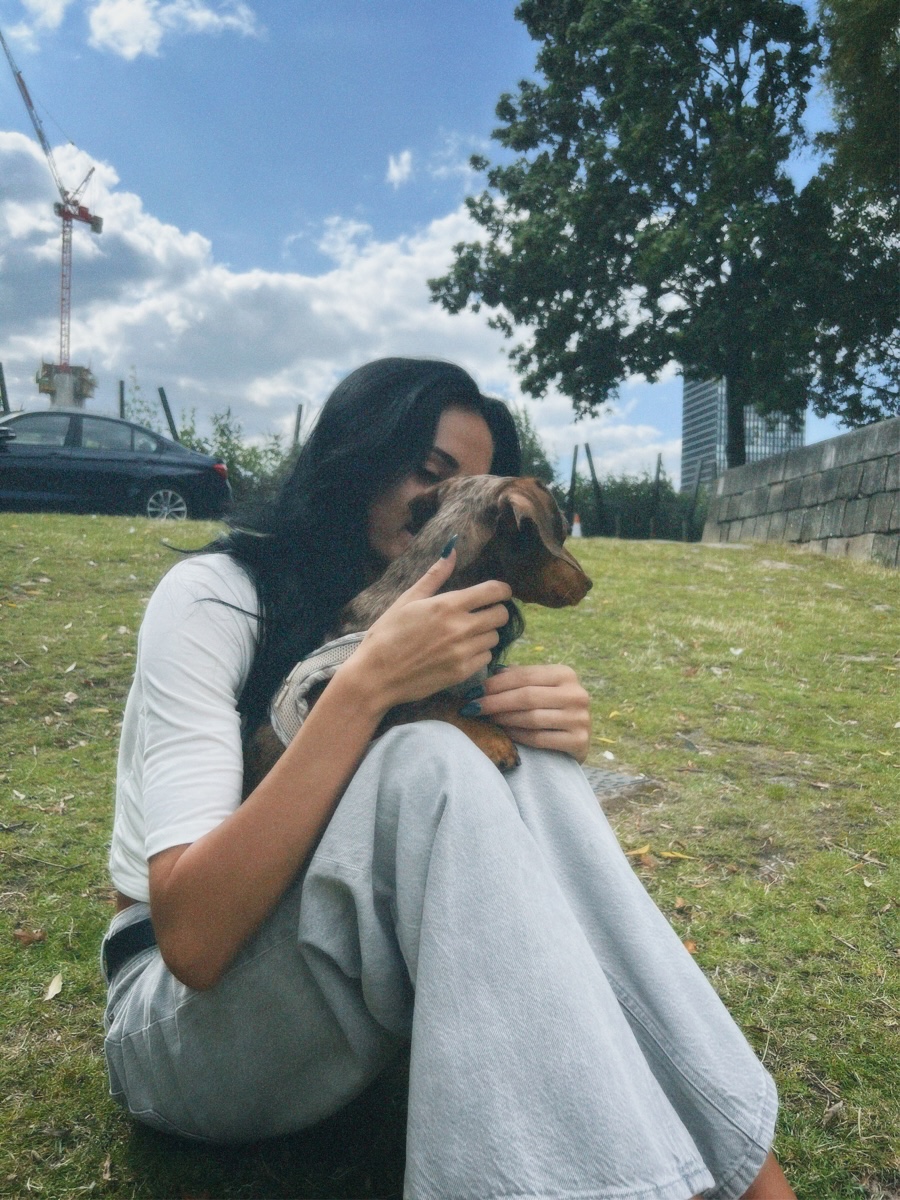 Lucy sitting on the grass hugging a dachshund, with a Manchester crane and city buildings behind